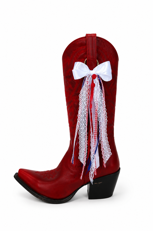 A red western cowboy boot decorated with a white bow, white lace, and red and white striped ribbon tassels, shown against a plain white background.